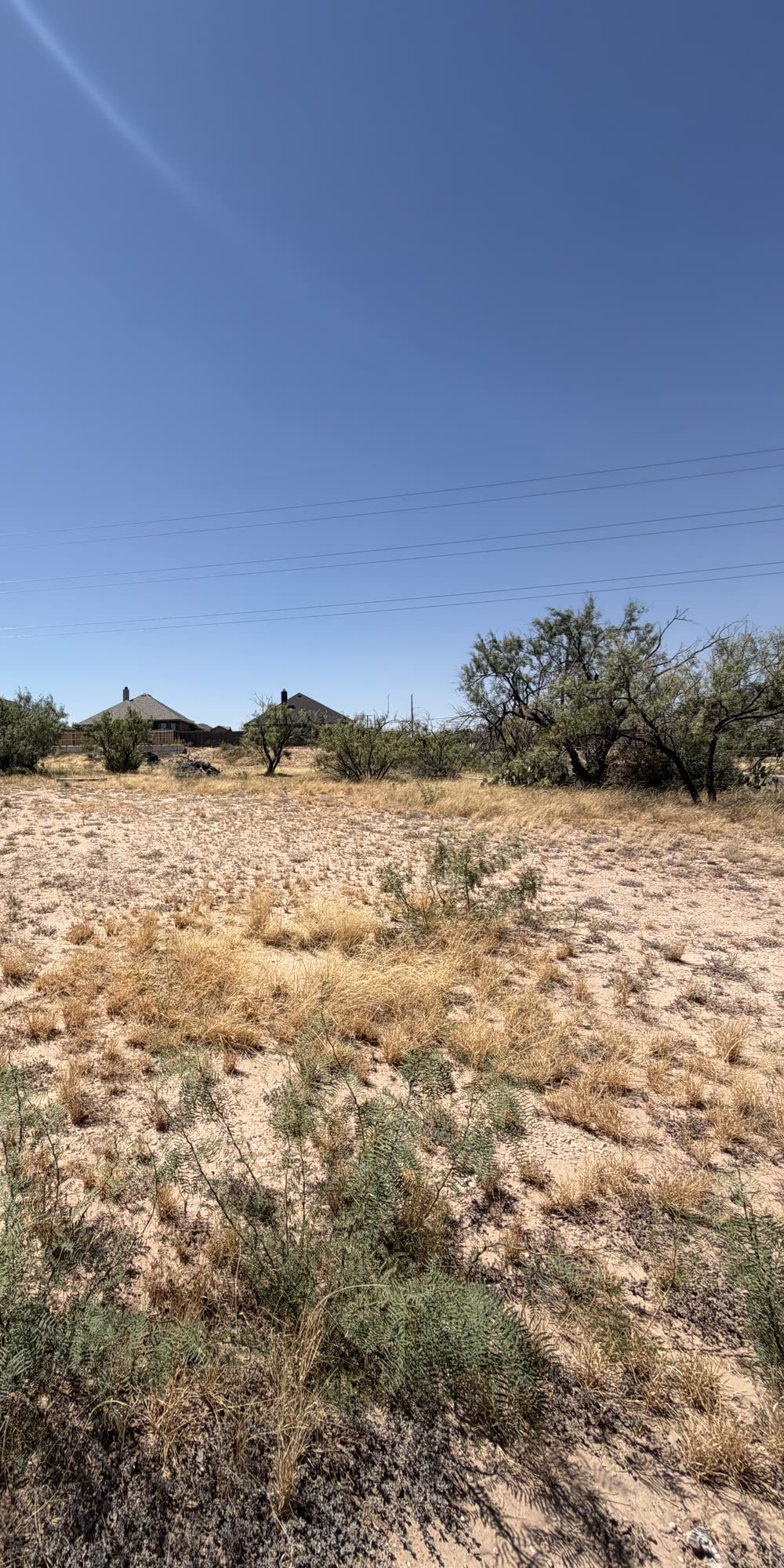 Vacant lot at 700 Baylor Blvd in Big Spring, Texas, seen from a high angle over sandy ground and mesquite shrubs